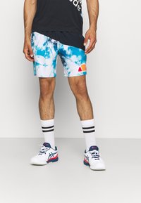 Pánské plavky s modro-bílým tie-dye vzorem, elastickým pasem a logem. V kombinaci s bílými botami a pruhovanými ponožkami.