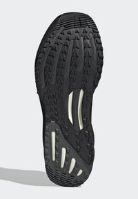 Sort gummisåle med en tekstureret overflade, der har dybe riller for greb samt hvide polstringsdetaljer integreret i designet.