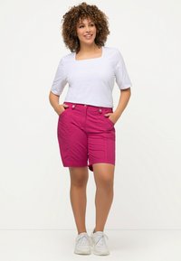 Roze shorts met knoopsluiting en zijzakken, gecombineerd met een aansluitend wit topje met vierkante halslijn. Model draagt witte sneakers.