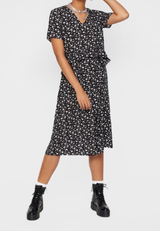 Femme portant une robe midi noire à imprimé floral blanc, des chaussettes blanches aux chevilles, des bottes noires à plateforme à lacets et des colliers argentés superposés.