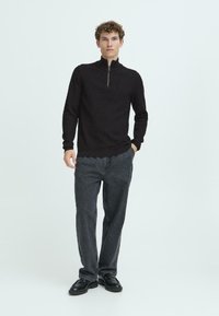 Pullover nero a coste con colletto alto e zip parziale frontale. Abbinato a jeans larghi scuri e scarpe nere. Tessuto morbido.