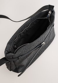 Melnas teksturētas ādas plecu soma ar rāvējslēdzēja aizdari, iekšpusē gluda oderējuma un ārpusē rāvējslēdzēja kabata.