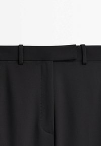 Pantalon noir à texture lisse, avec une ceinture plate, des passants de ceinture et une poche latérale avec un détail de couture subtile.