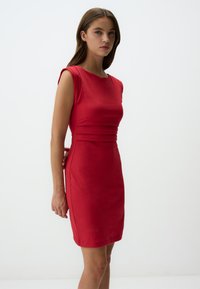Abito rosso aderente con maniche corte, caratterizzato da dettagli arricciati in vita e una superficie liscia. Design semplice e lineare.