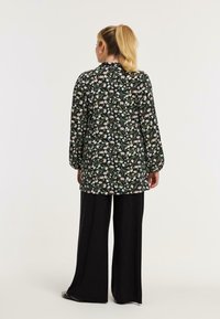 Zwart tuniek met bloemenmotief, lange mouwen en hoge kraag, gecombineerd met wijde zwarte broek. Lichte, relaxed fit.