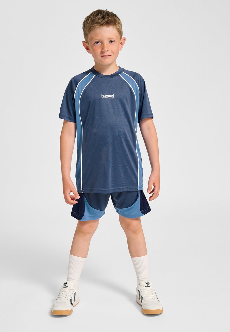 Marinstil sport t-shirt med ljusblå detaljer; kombinerad med matchande shorts. Har fukttransporterande tyg och en avslappnad passform. Vita sneakers och strumpor.