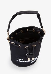 Sac en toile noire avec quincaillerie dorée, fermeture à cordon, et inscription imprimée "JE SUIS UN SAC RESPONSABLE" sur l'extérieur.