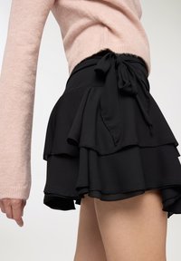 Gonna nera a strati con balze, tessuto leggero e dettaglio in vita annodato; presenta una texture liscia e sottili cuciture decorative.