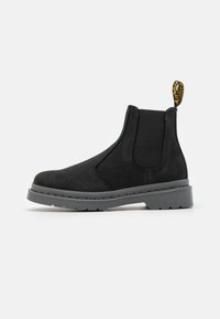 Bottines Chelsea en suède noir avec semelle en caoutchouc gris, panneaux latéraux élastiques et une languette. Présente une finition texturée et des détails de couture minimaux.