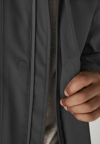 Gray waterproof jacket with a smooth texture, featuring a zipper, snap buttons, and a contrasted inner layer visible at the collar.