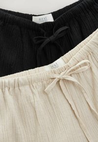 Pantaloni leggeri in lino nere e crema con vita elasticizzata e lacci. Tessuto testurizzato con pieghe arricciate. Etichette visibili.