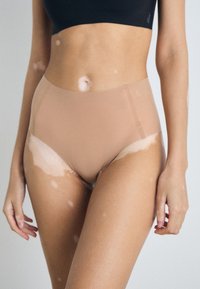High-waisted, nude-colored underwear made from smooth, stretchy material, featuring a seamless design and minimalistic detailing.