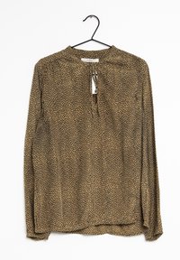 Blusa marrone a maniche lunghe con motivo a pois neri, dotata di chiusura con apertura a cuore sul retro e tessuto morbido e trasparente. Appesa a un gancio nero.