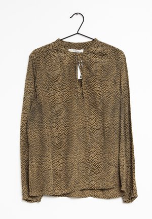 Blouse marron à manches longues avec un motif à pois noirs, dotée d'une fermeture dos en trou de serrure et en tissu doux et transparent. Accrochée à un crochet noir.