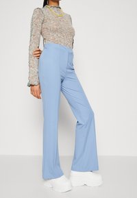 Jasnoniebieskie, szerokie spodnie wykonane z gładkiej tkaniny, z wysokim stanem i gładkimi plisami z przodu, zestawione z masywnymi białymi butami na platformie.