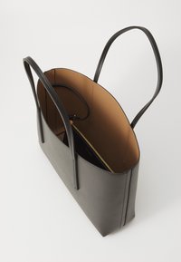 Grå totebag med lange håndtak, sett fra oven; har et brunt interiør og en glidelåslomme synlig inni.