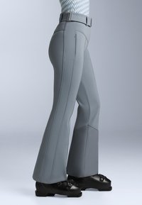 Grå utsvängda byxor med en slät textur, som har kontrasterande sömmar, sidoficka med dragkedja och en bred midja. Bärs med svarta skor.