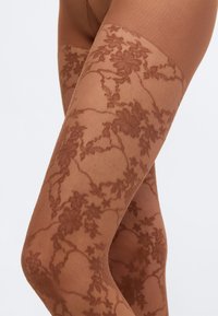 Δαντέλινες καλτσοδέτες μέχρι το μηρό σε θερμό καφέ χρώμα, με λουλουδένια σχέδια, διαφανή υφή και λείο επάνω λάστιχο για άνεση και εφαρμογή.