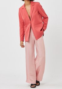 Korallblazer med slagkrage, en knappstängning och två framfickor. Matchas med ljusrosa vida byxor och svarta sandaler.