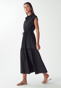 Musternik puhvahib tihedus plave vestukar, nupud esifront. Silgutav talje ja kihiline seelik. Mudel kannab lamedaid rihmadega sandaale. Sile ja kerge kangas.