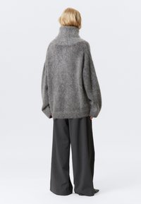 Pulover gri supradimensionat cu guler înalt, fabricat dintr-un material moale și pufos. Asortat cu pantaloni largi de culoare închisă, creând o siluetă relaxată.