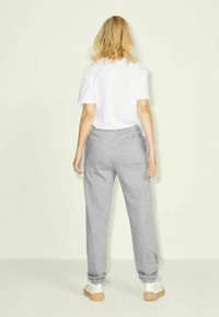 Grå sweatpants med elastisk midjeband och muddade anklar, ihop med en vit t-shirt. Minimalistisk design, avslappnad passform.