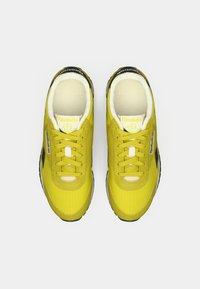 Par žutih Reebok tenisica s crnim i bijelim akcentima, dizajnom s vezicama i mekanim puhaljivim unutrašnjostima, prikazanih iz ptičje perspektive na bijeloj pozadini.