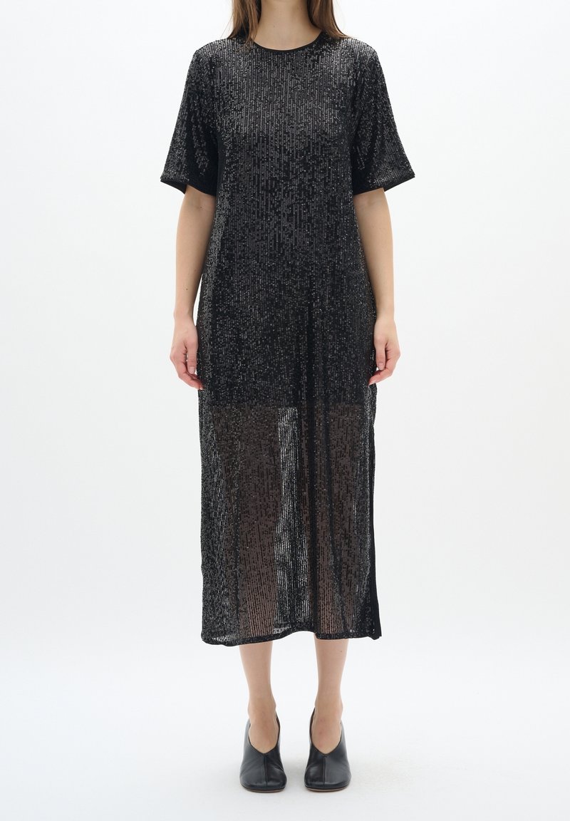 Svart paljett-midi klänning med korta ärmar, med en genomskinlig nedre del och en rak silhuett. Mjuk, texturerad tyg med glänsande detaljer.