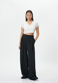 Hvid cropped V-hals t-shirt parret med løse, højtaljede sorte bukser med folder og en glat, flydende tekstur.