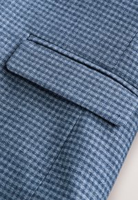 Blue textured fabric featuring a small checkered pattern, with a neatly folded pocket detail on the left side.