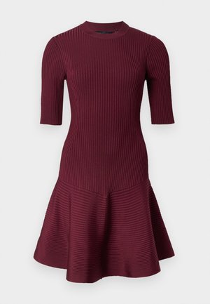 Bordeaux ribbeljurk met korte mouwen, aansluitend lijfje en uitlopende rok. Voorzien van een ronde hals en textuurstof.