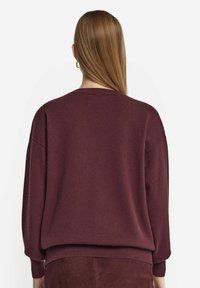 Bordeauxfarbener Strickpullover mit lockerer Passform, überschnittenen Schultern und geripptem Saum. Sanfte Textur, lange Ärmel und runder Halsausschnitt. Rückansicht dargestellt.