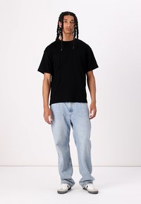 Tricou negru cu mânecă scurtă, croială lejeră, asortat cu blugi evazați de culoare albastră deschisă. Încălțămintea are un design gri și alb, dotată cu șireturi.