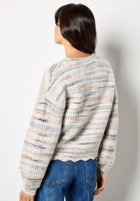 Sweter robiony na drutach w pastelowych kolorach z pionowymi paskami, prążkowaną strukturą i falbaniastym dołem. Posiada okrągły dekolt i luźny krój.