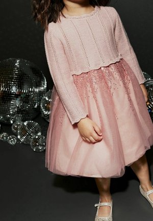 Pull rose en tricot à manches longues, superposé sur une robe en tulle rose clair ornée de sequins, associé à des ballerines brillantes.