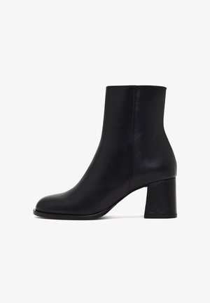 Botín de cuero negro con textura suave, punta redondeada y tacón grueso. Presenta un diseño elegante y minimalista.