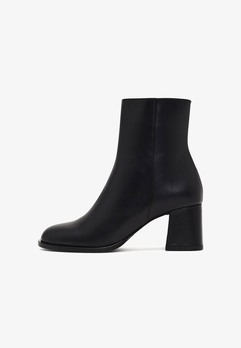 Bottine en cuir noir avec une texture lisse, bout arrondi et un talon bloc épais. Présente un design élégant et minimaliste.