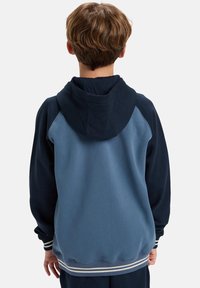 Blauwe en marineblauwe hoodie met een lange pasvorm, raglanmouwen en een voorzak. Bevat een gestructureerde oppervlakte en gestreepte zoomdetails.