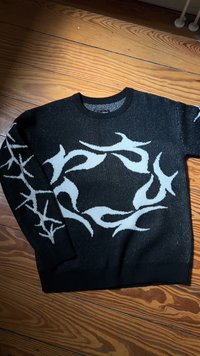 Suéter de malha preto com um padrão abstrato branco na frente e nas mangas. Gola redonda e punhos e bainha canelados. Textura suave.