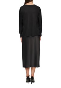 Schwarzes Langarmoberteil mit Rundhalsausschnitt, kombiniert mit einem schwarzen Midikleid und hohen Schuhen. Glatte Textur und simples Design.