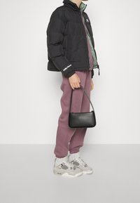 Svart puffjacka med grön foder, lila joggerByxor, grå sneakers med meshdetaljer och en liten svart handväska. Avslappnad outfit.