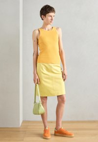 Gul ribbet tanktop, lys gul skjørt, oransje joggesko og en grønn veske. Glatte teksturer, tettsittende design og klare farger.