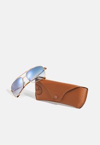 Occhiali da sole aviator in metallo dorato con lenti blu sfumate, posati accanto a una custodia in pelle marrone con chiusura a scatto e logo impresso.
