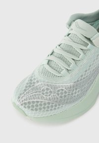 Baskets de sport vert menthe clair avec une tige en maille respirante, un design texturé et une semelle lisse légèrement courbée avec des accents argentés.