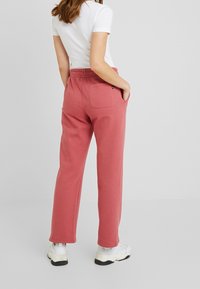 Roze sweatpants met een elastische tailleband en zijzakken, gemaakt van zachte stof. Heeft een enkele achterzak. Gestyled met een witte top.