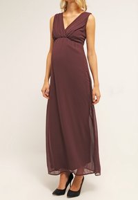 Graviditets maxi klänning i djup burgundyröd, med en plisserad V-ringning, ärmlös design och mjukt, flödande tyg med en sidoslits.