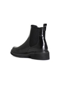 Botas Chelsea negras con un acabado brillante, paneles laterales elásticos, tirador y una suela de goma negra resistente. Costuras detalladas alrededor de la suela.