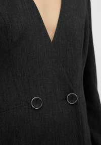 Zwarte blazer met een diepe V-hals, dubbelzijdig ontwerp, gestructureerde stof en ronde zilverkleurige knopen.