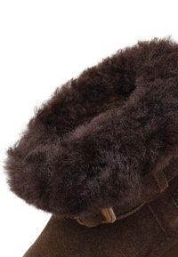 Braune Wildleder-Ankle-Boots mit einem flauschigen braunen Fellkragen und einem Metallverschluss-Detail. Die strukturierten Oberflächen verleihen ein warmes, gemütliches Erscheinungsbild.