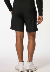 Sorte atletiske shorts med elastisk talje, sidelommer og en bagtilsiddende lynlåslomme, parret med hvide høj-top sneakers.